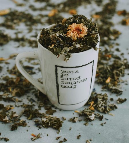 A close-up of an herbal tea mug filled with dried leaves and flowers on a table.